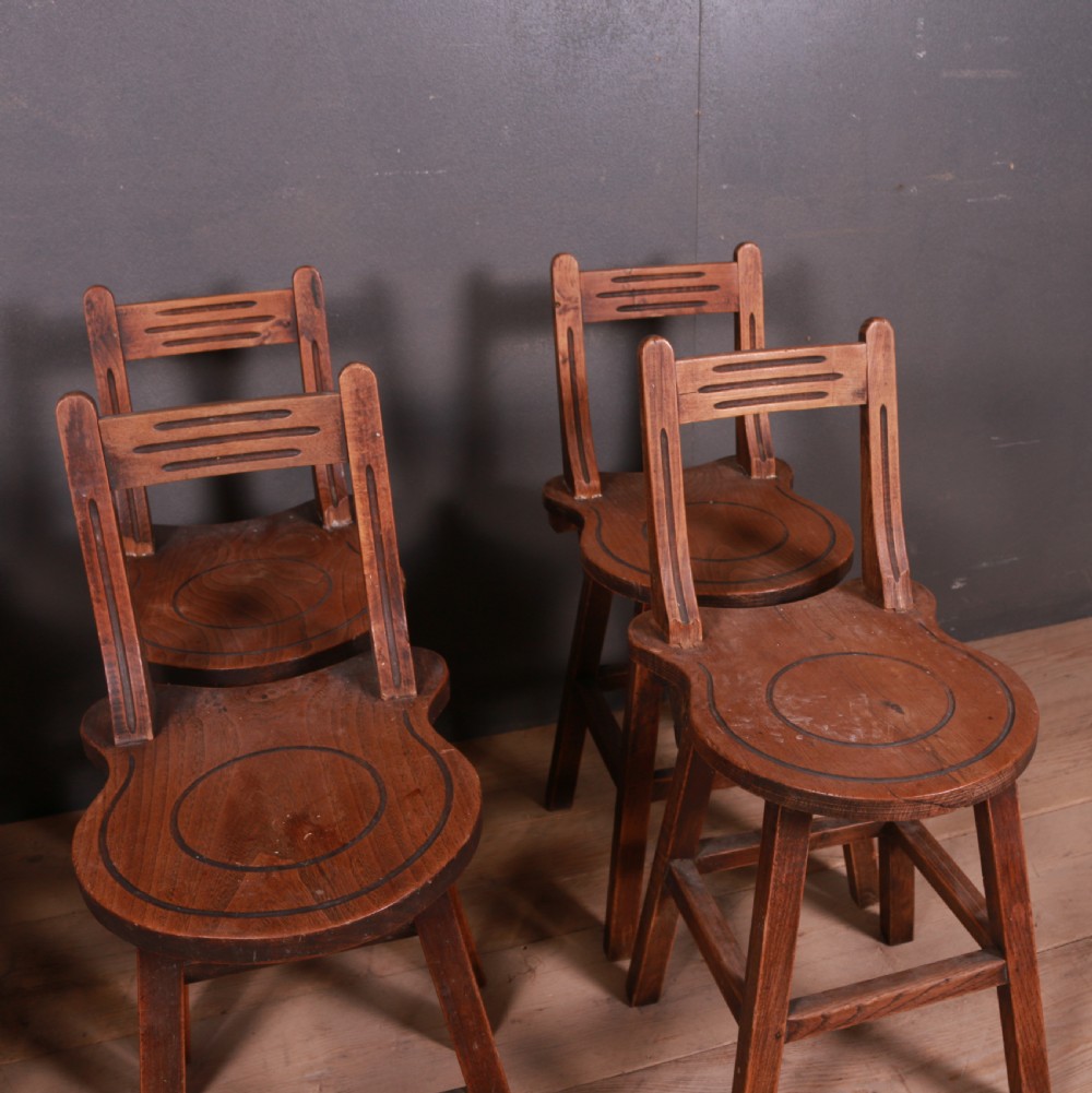 A set of six warm brown Swiss elm back stools featuring pierced top crest rails, circular carved seat details, and splayed legs with stretchers. View IV