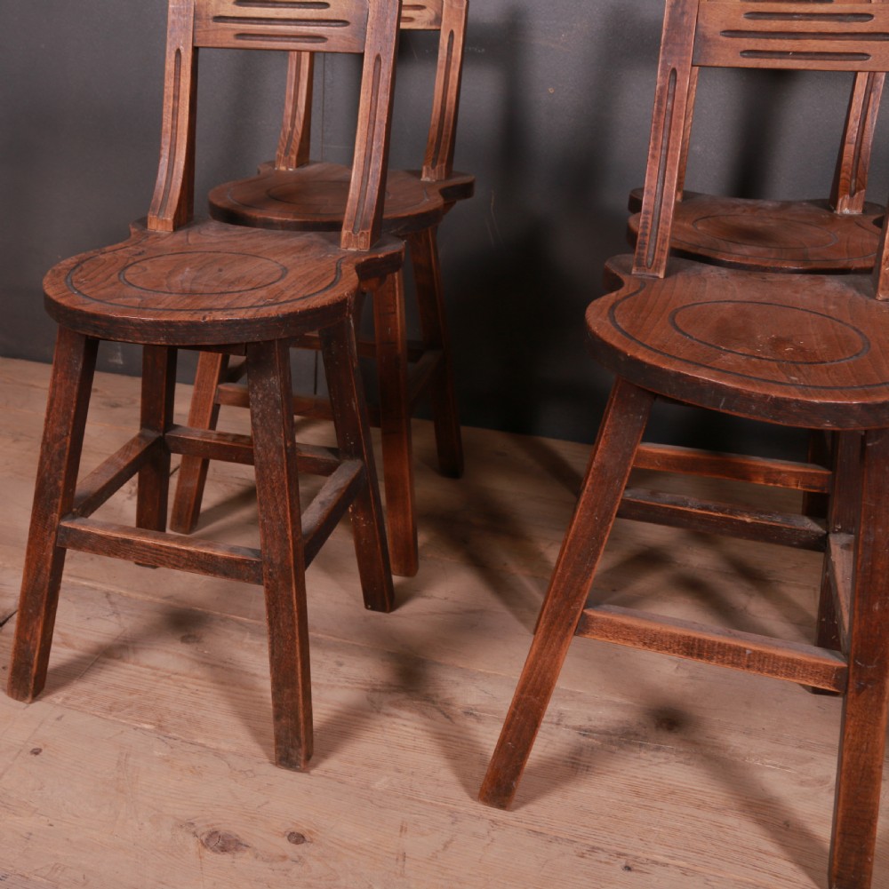 A set of six warm brown Swiss elm back stools featuring pierced top crest rails, circular carved seat details, and splayed legs with stretchers. View V