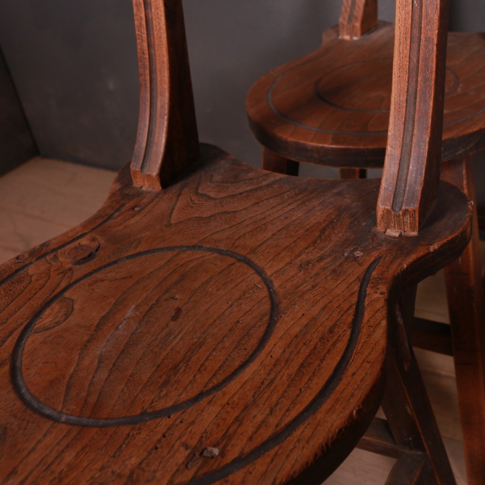 A set of six warm brown Swiss elm back stools featuring pierced top crest rails, circular carved seat details, and splayed legs with stretchers. View VI