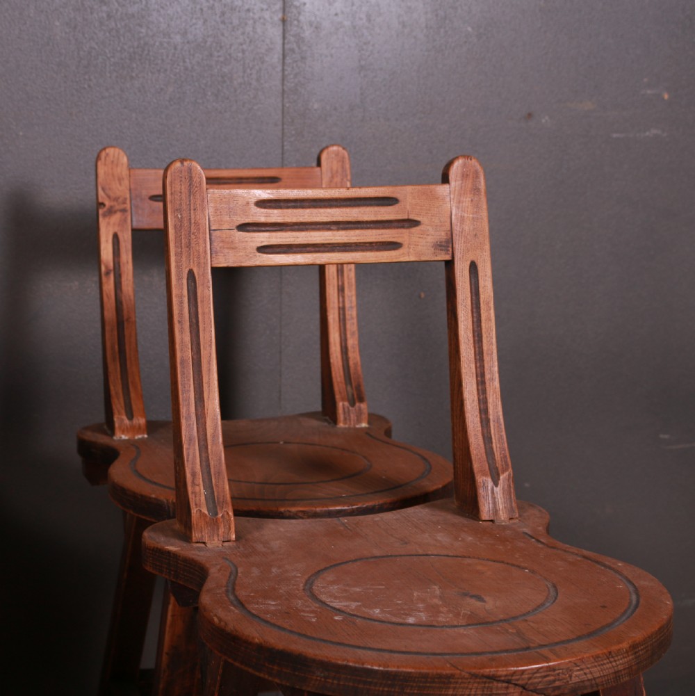 A set of six warm brown Swiss elm back stools featuring pierced top crest rails, circular carved seat details, and splayed legs with stretchers. View VII