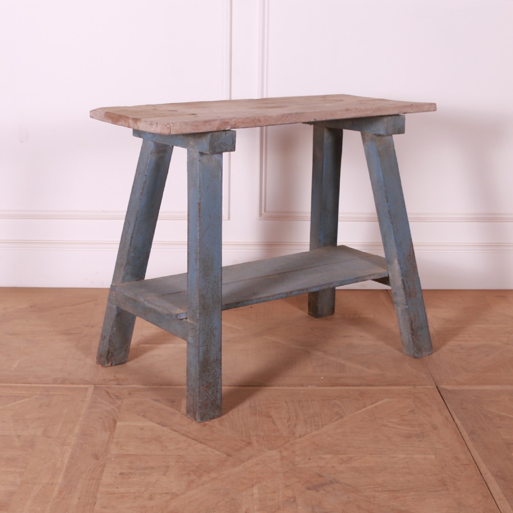 A rustic pine trestle table featuring a natural unpainted wood top and distressed blue painted A-frame legs with a lower storage shelf.