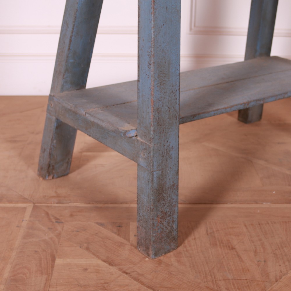 A rustic pine trestle table featuring a natural unpainted wood top and distressed blue painted A-frame legs with a lower storage shelf. View II