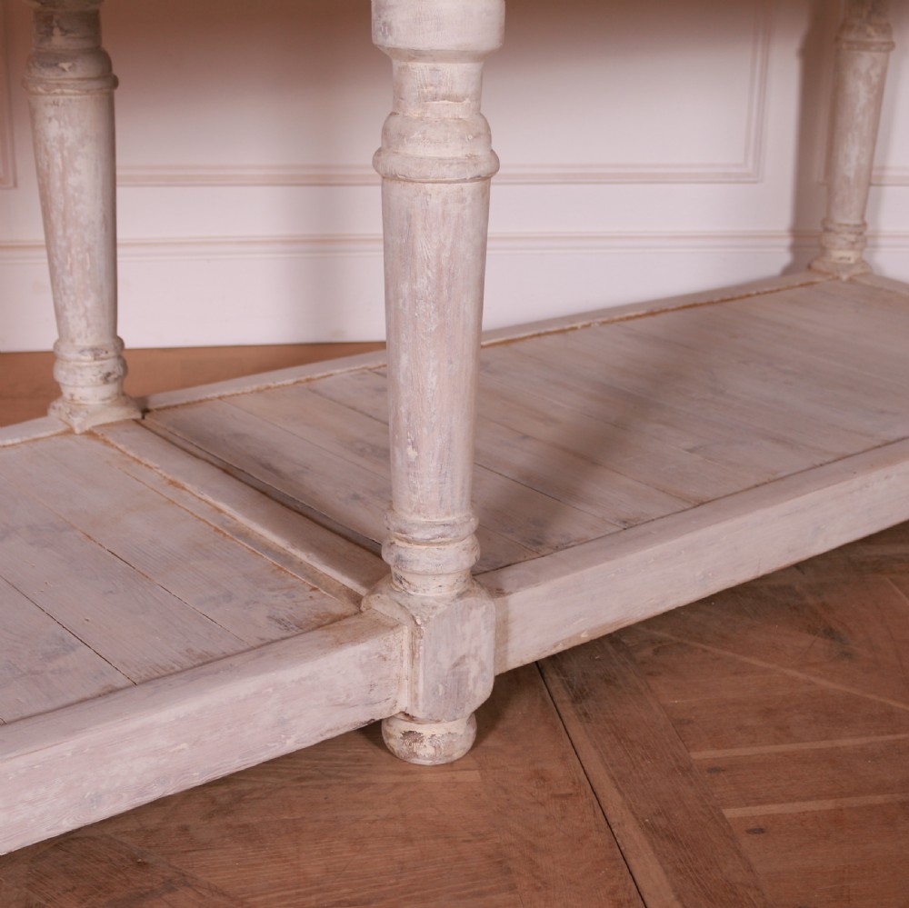 A long French painted drapers table featuring a natural wood top, six turned legs, a distressed white paint finish, and a full-length lower shelf. View V