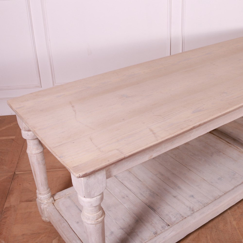 A long French painted drapers table featuring a natural wood top, six turned legs, a distressed white paint finish, and a full-length lower shelf. View VI