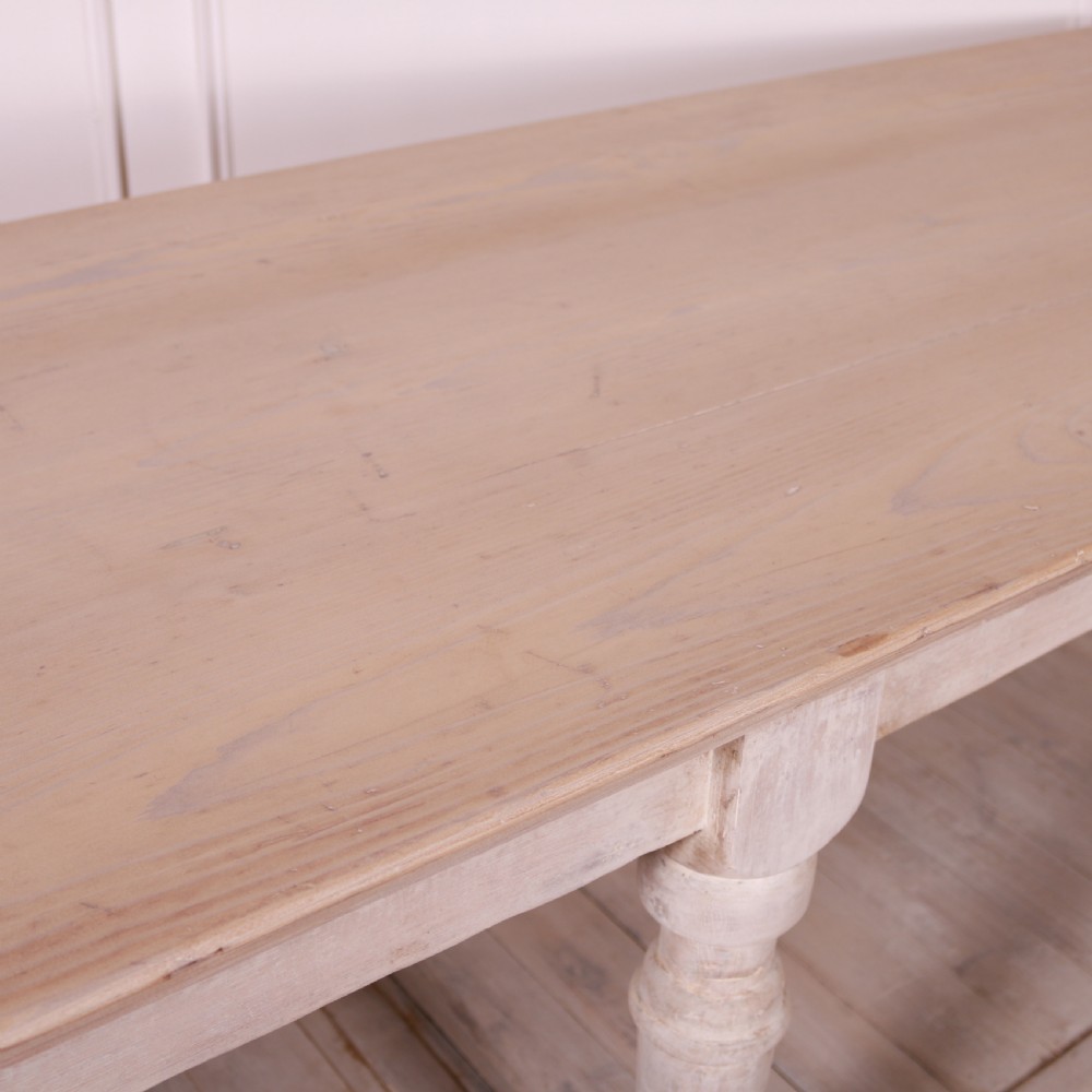 A long French painted drapers table featuring a natural wood top, six turned legs, a distressed white paint finish, and a full-length lower shelf. View VII