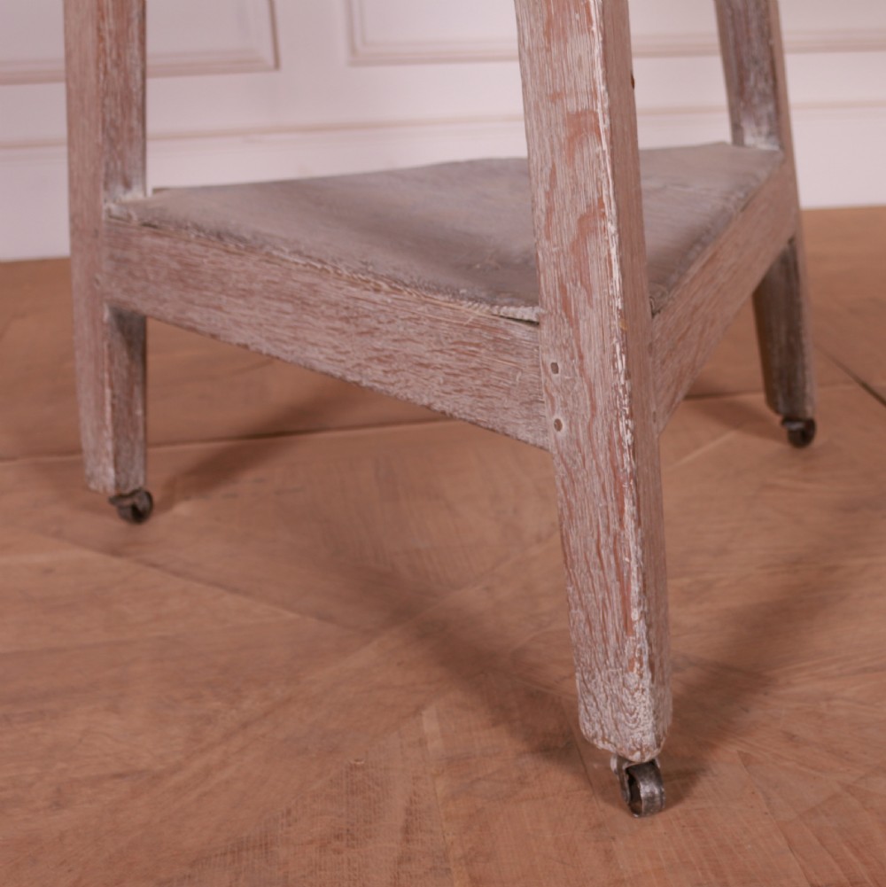 A three-legged bleached oak cricket table featuring a circular top, a triangular lower shelf, and small castors on the feet. View II