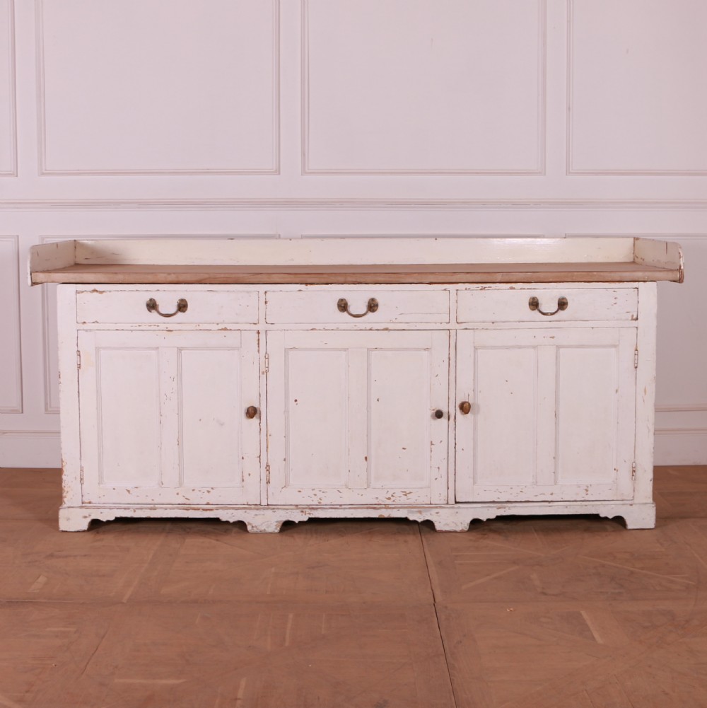 A Scottish painted pine dresser base with three top drawers over three panelled cupboard doors, featuring a natural timber top with a low gallery back and a distressed off-white painted finish.
