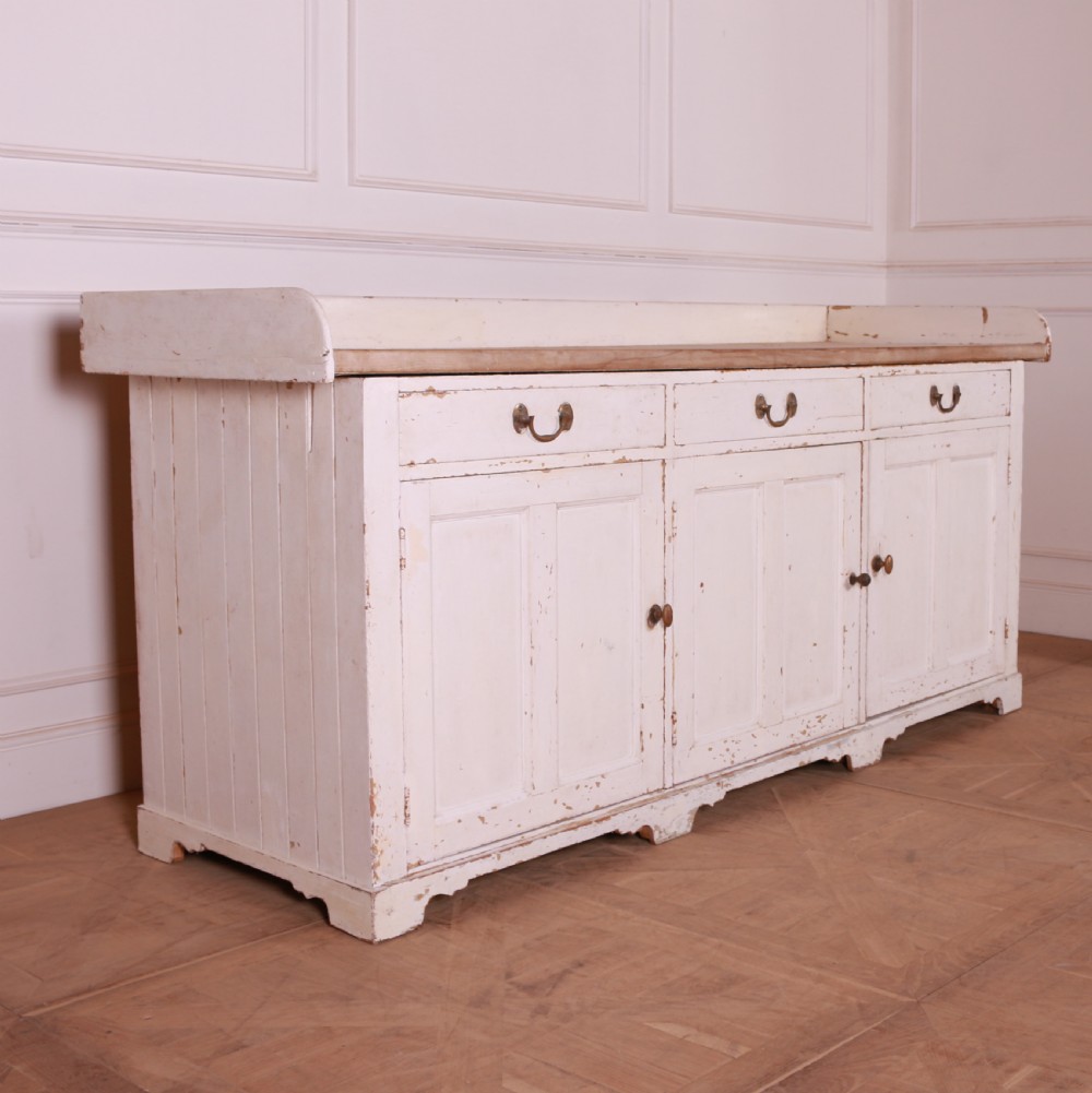 A Scottish painted pine dresser base with three top drawers over three panelled cupboard doors, featuring a natural timber top with a low gallery back and a distressed off-white painted finish. View II