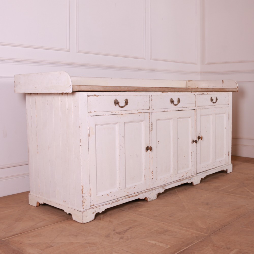 A Scottish painted pine dresser base with three top drawers over three panelled cupboard doors, featuring a natural timber top with a low gallery back and a distressed off-white painted finish. View III