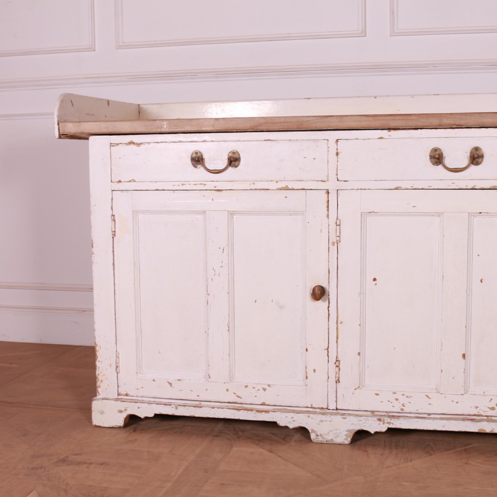 A Scottish painted pine dresser base with three top drawers over three panelled cupboard doors, featuring a natural timber top with a low gallery back and a distressed off-white painted finish. View IV