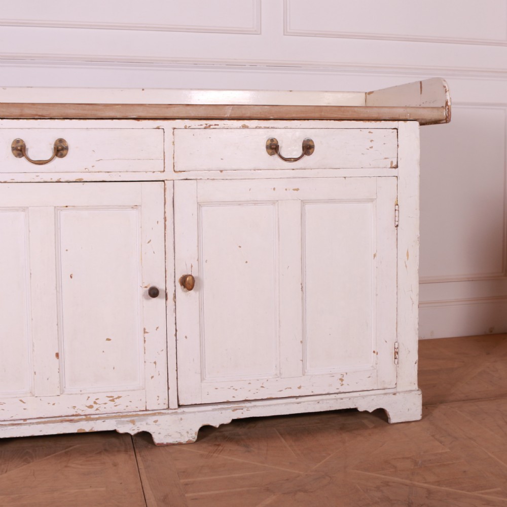 A Scottish painted pine dresser base with three top drawers over three panelled cupboard doors, featuring a natural timber top with a low gallery back and a distressed off-white painted finish. View V