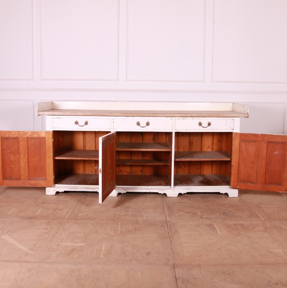 A Scottish painted pine dresser base with three top drawers over three panelled cupboard doors, featuring a natural timber top with a low gallery back and a distressed off-white painted finish. View IX