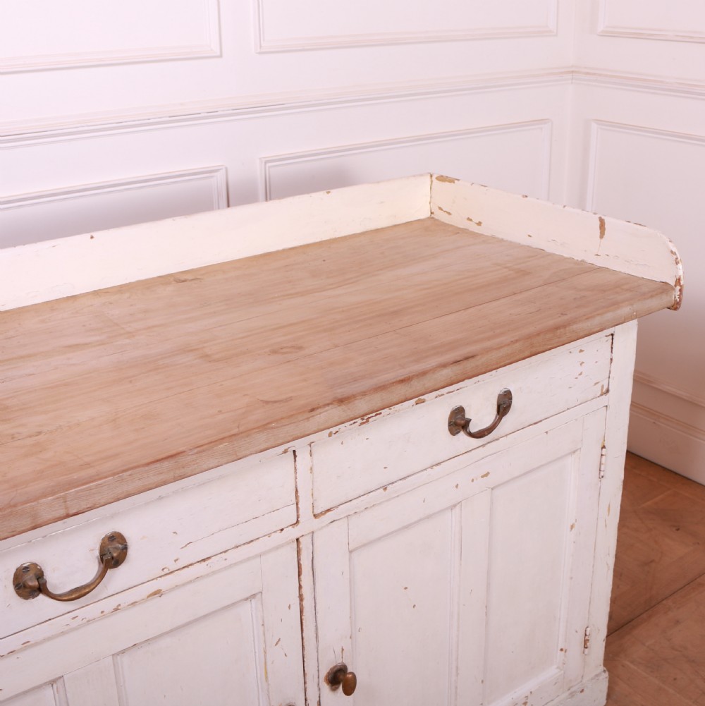 A Scottish painted pine dresser base with three top drawers over three panelled cupboard doors, featuring a natural timber top with a low gallery back and a distressed off-white painted finish. View X
