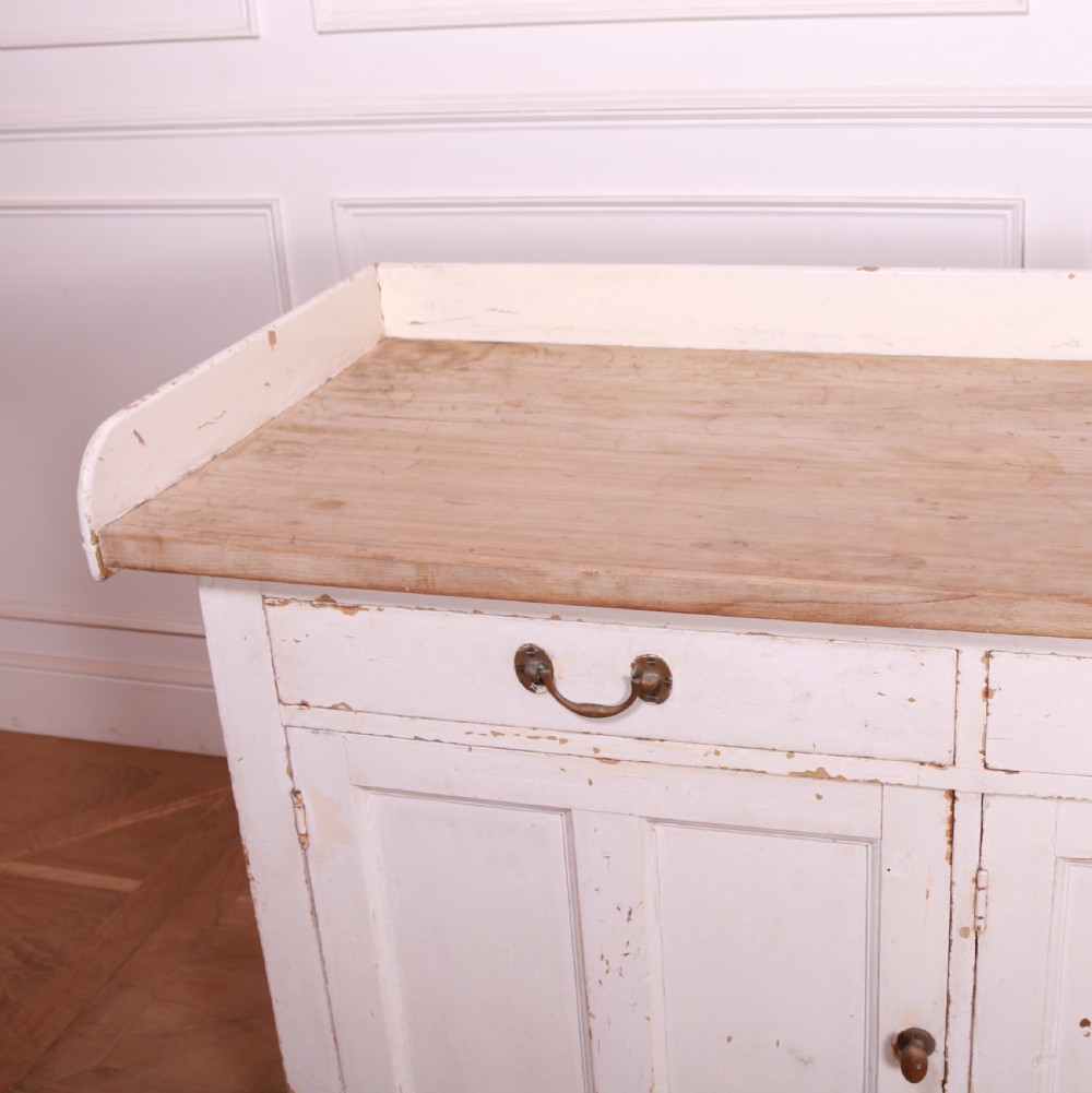 A Scottish painted pine dresser base with three top drawers over three panelled cupboard doors, featuring a natural timber top with a low gallery back and a distressed off-white painted finish. View XI