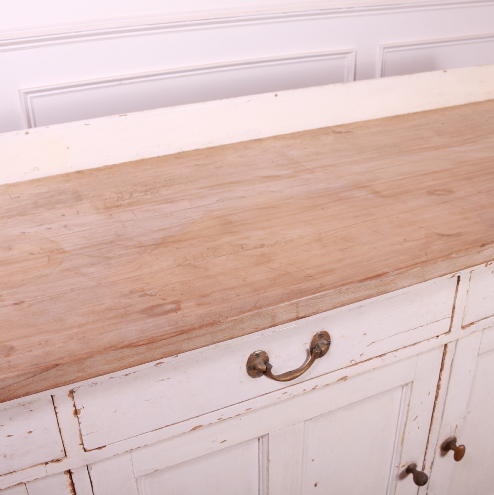 A Scottish painted pine dresser base with three top drawers over three panelled cupboard doors, featuring a natural timber top with a low gallery back and a distressed off-white painted finish. View XII