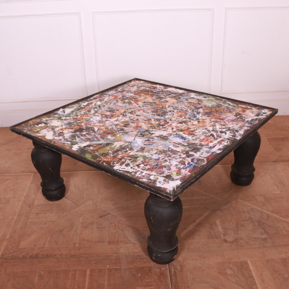 A large low square coffee table featuring heavy turned black legs and a colourful collage pattern inset into the tabletop surface. View III