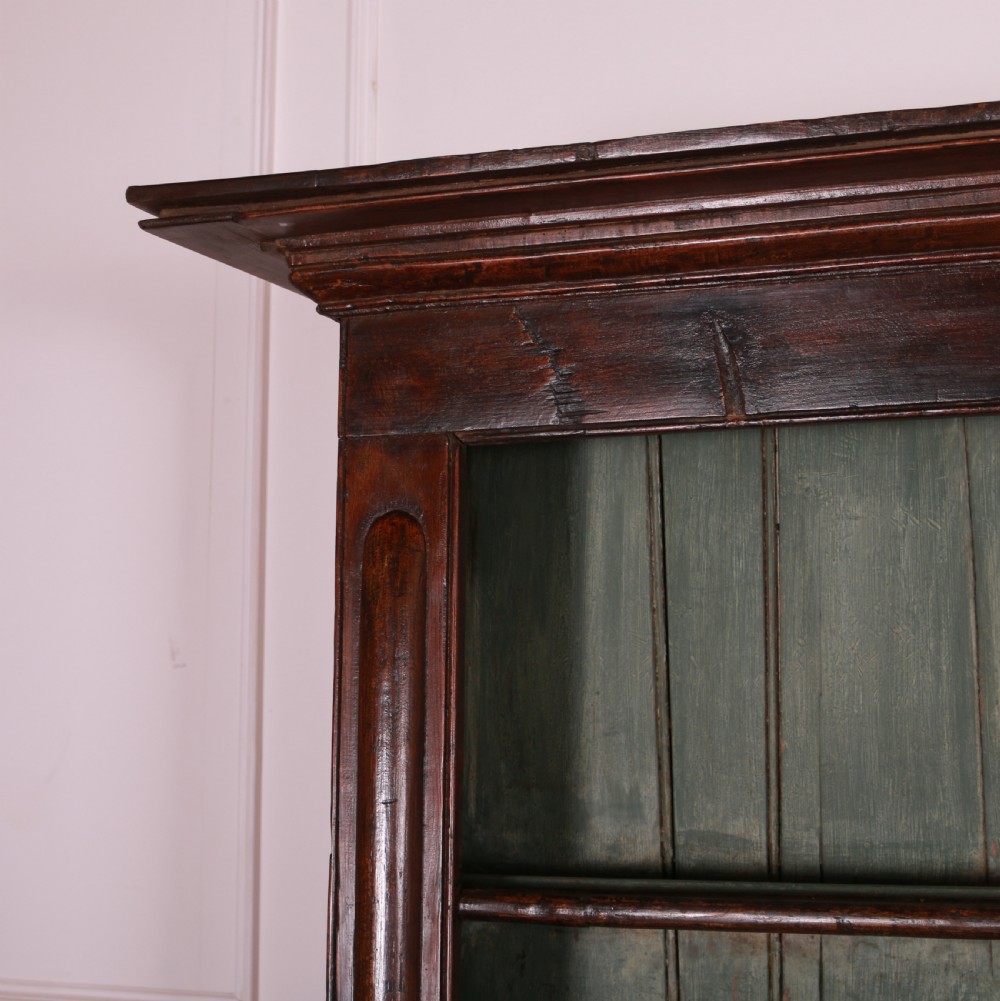A dark pine kitchen dresser featuring an open three-tier plate rack with a sage green painted backboard above a base with three central drawers and two panelled side cupboards. View IV