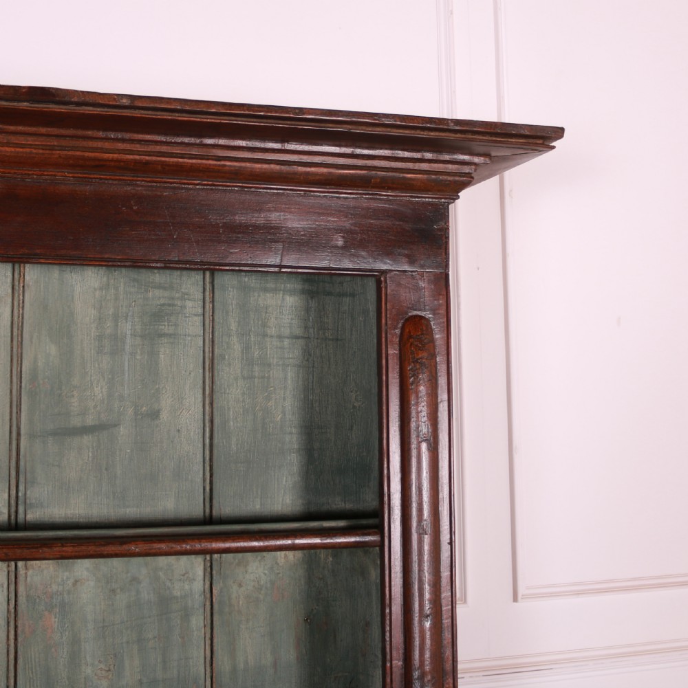 A dark pine kitchen dresser featuring an open three-tier plate rack with a sage green painted backboard above a base with three central drawers and two panelled side cupboards. View V