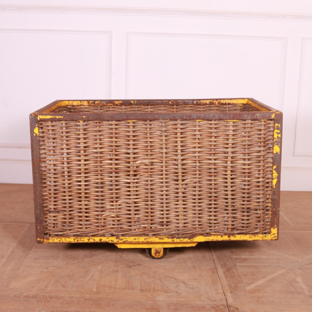 A large rectangular woven wicker basket enclosed in a distressed yellow painted steel frame with small castors on the base. View II