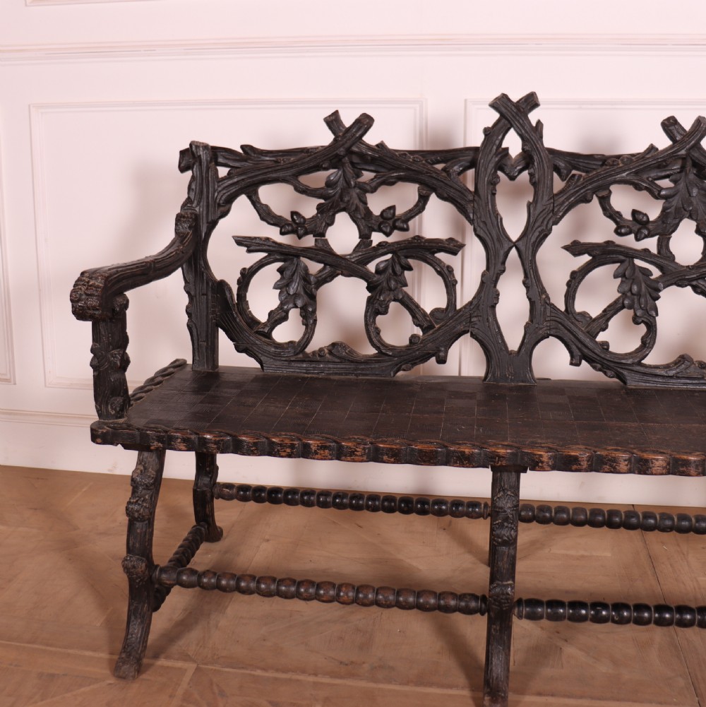A dark wood Victorian bench with intricate branch and leaf carvings on the backrest, carved armrests, a textured seat, and bobbin stretchers. View II
