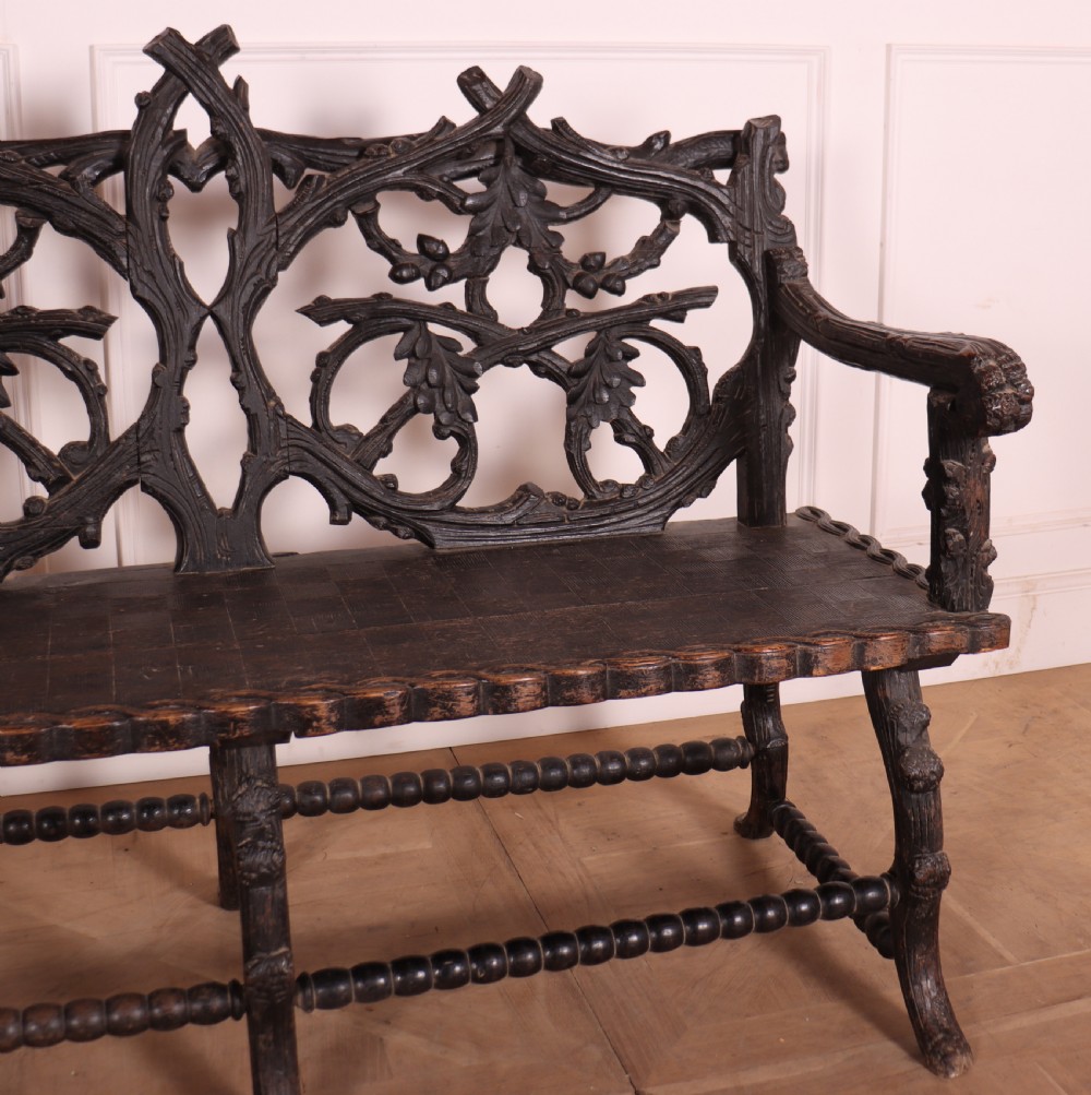 A dark wood Victorian bench with intricate branch and leaf carvings on the backrest, carved armrests, a textured seat, and bobbin stretchers. View III
