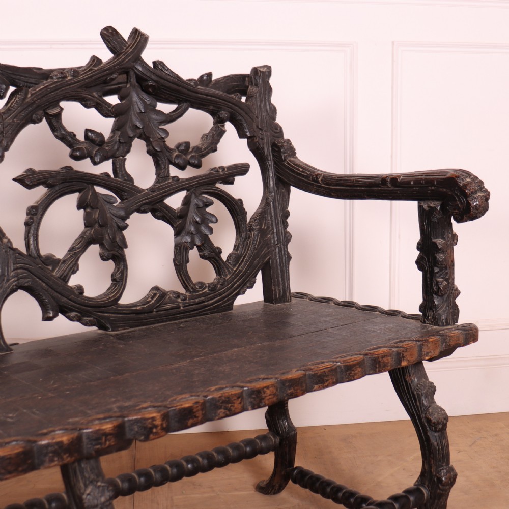 A dark wood Victorian bench with intricate branch and leaf carvings on the backrest, carved armrests, a textured seat, and bobbin stretchers. View VIII