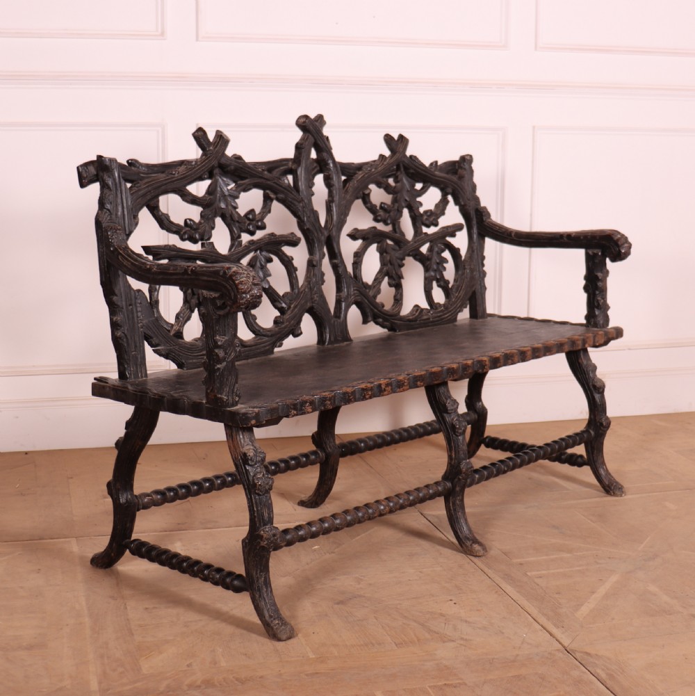 A dark wood Victorian bench with intricate branch and leaf carvings on the backrest, carved armrests, a textured seat, and bobbin stretchers. View XI