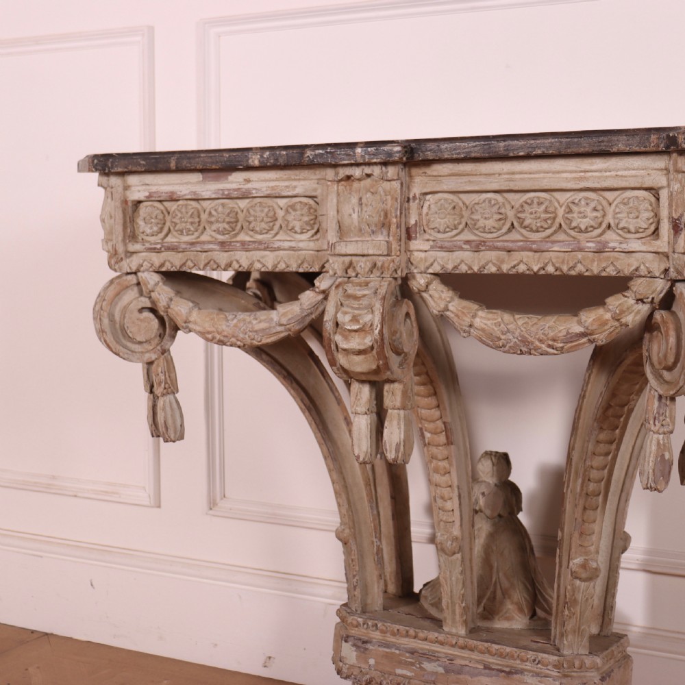 An 18th-century French carved wood console table featuring a dark top, rosette frieze, carved drapery swags, and a distressed off-white finish. View II