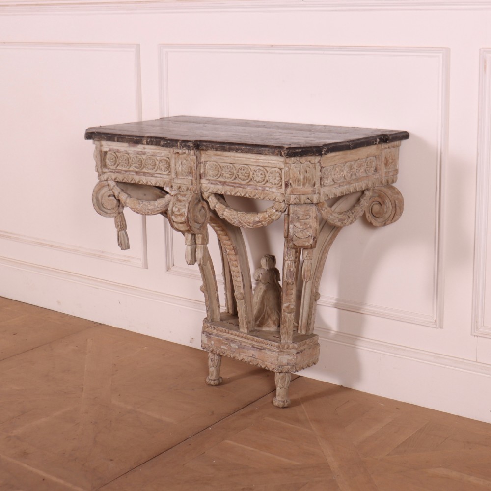 An 18th-century French carved wood console table featuring a dark top, rosette frieze, carved drapery swags, and a distressed off-white finish. View IV