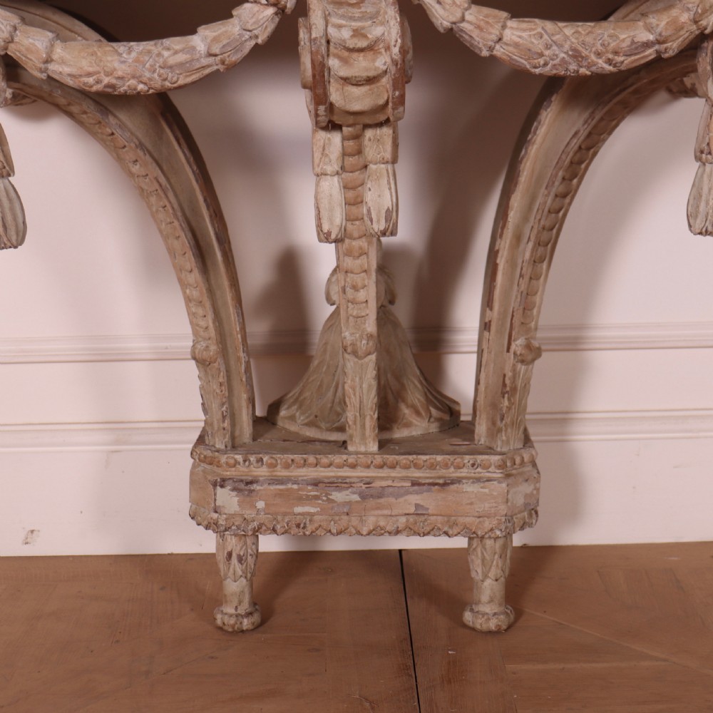 An 18th-century French carved wood console table featuring a dark top, rosette frieze, carved drapery swags, and a distressed off-white finish. View VIII