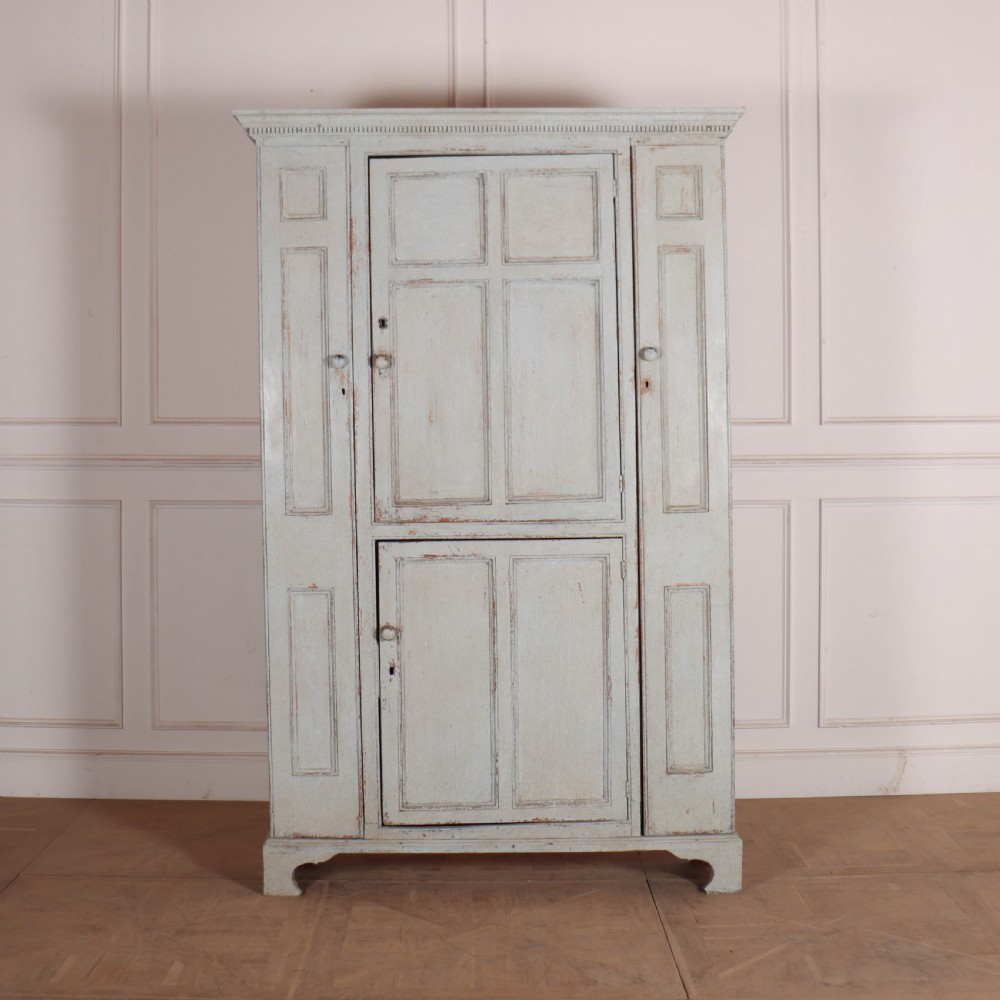 A small antique English housekeepers cupboard with a pale blue painted finish, panelled doors, turned wooden knobs, and bracket feet.