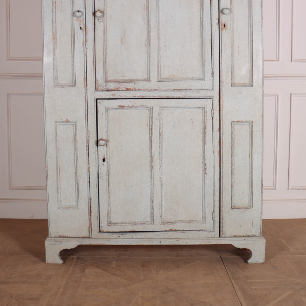 A small antique English housekeepers cupboard with a pale blue painted finish, panelled doors, turned wooden knobs, and bracket feet. View II