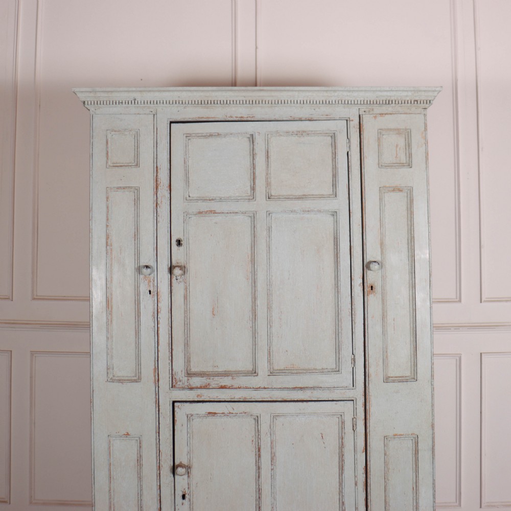 A small antique English housekeepers cupboard with a pale blue painted finish, panelled doors, turned wooden knobs, and bracket feet. View III
