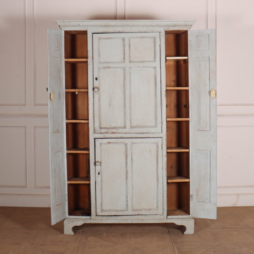 A small antique English housekeepers cupboard with a pale blue painted finish, panelled doors, turned wooden knobs, and bracket feet. View VII