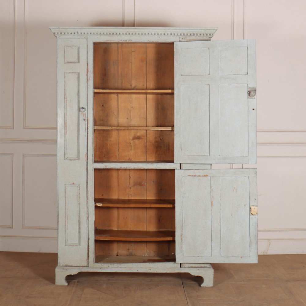 A small antique English housekeepers cupboard with a pale blue painted finish, panelled doors, turned wooden knobs, and bracket feet. View VIII