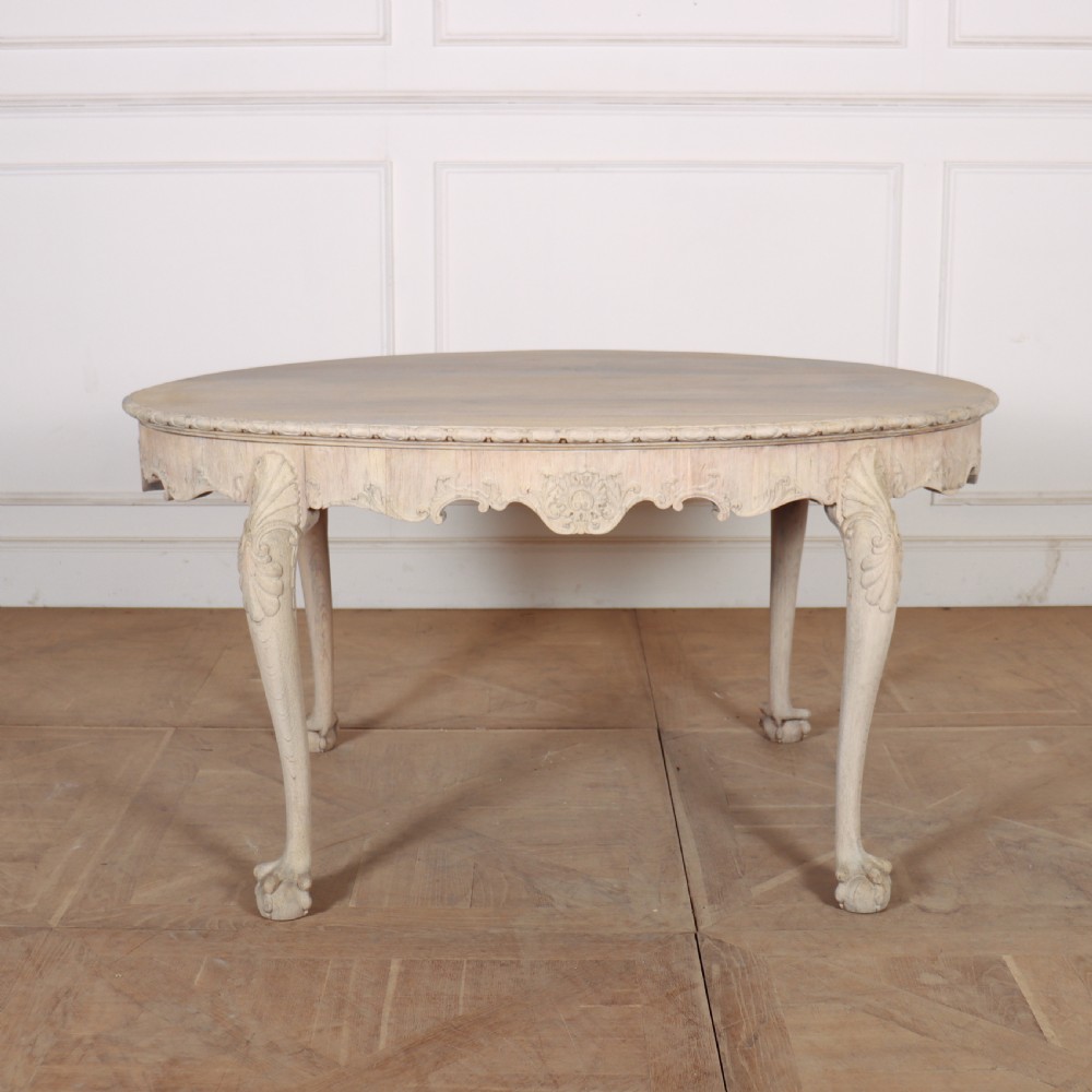 An antique bleached oak centre table with a carved apron, cabriole legs, and shell motifs resting on a parquet floor.