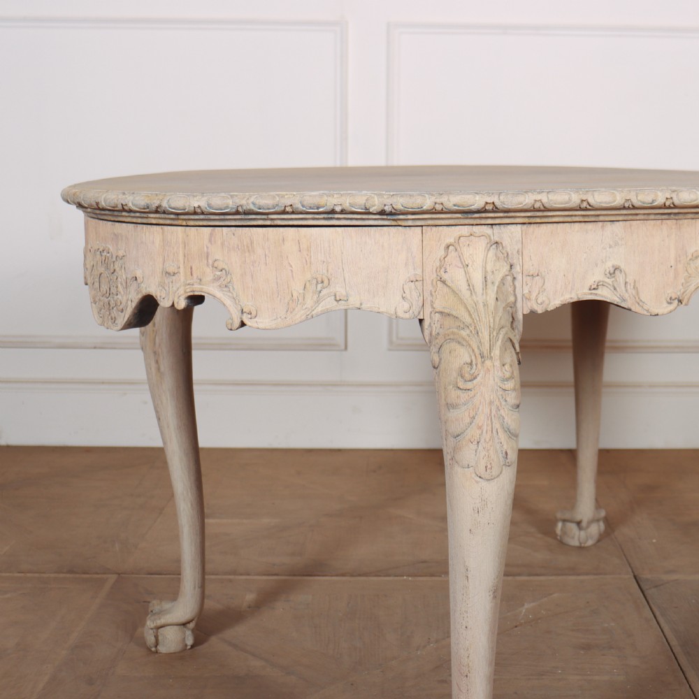 An antique bleached oak centre table with a carved apron, cabriole legs, and shell motifs resting on a parquet floor. View III