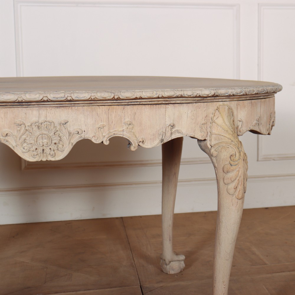 An antique bleached oak centre table with a carved apron, cabriole legs, and shell motifs resting on a parquet floor. View V