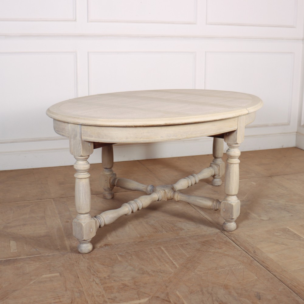 An oval bleached oak dining table with turned legs and an X-shaped lower stretcher.