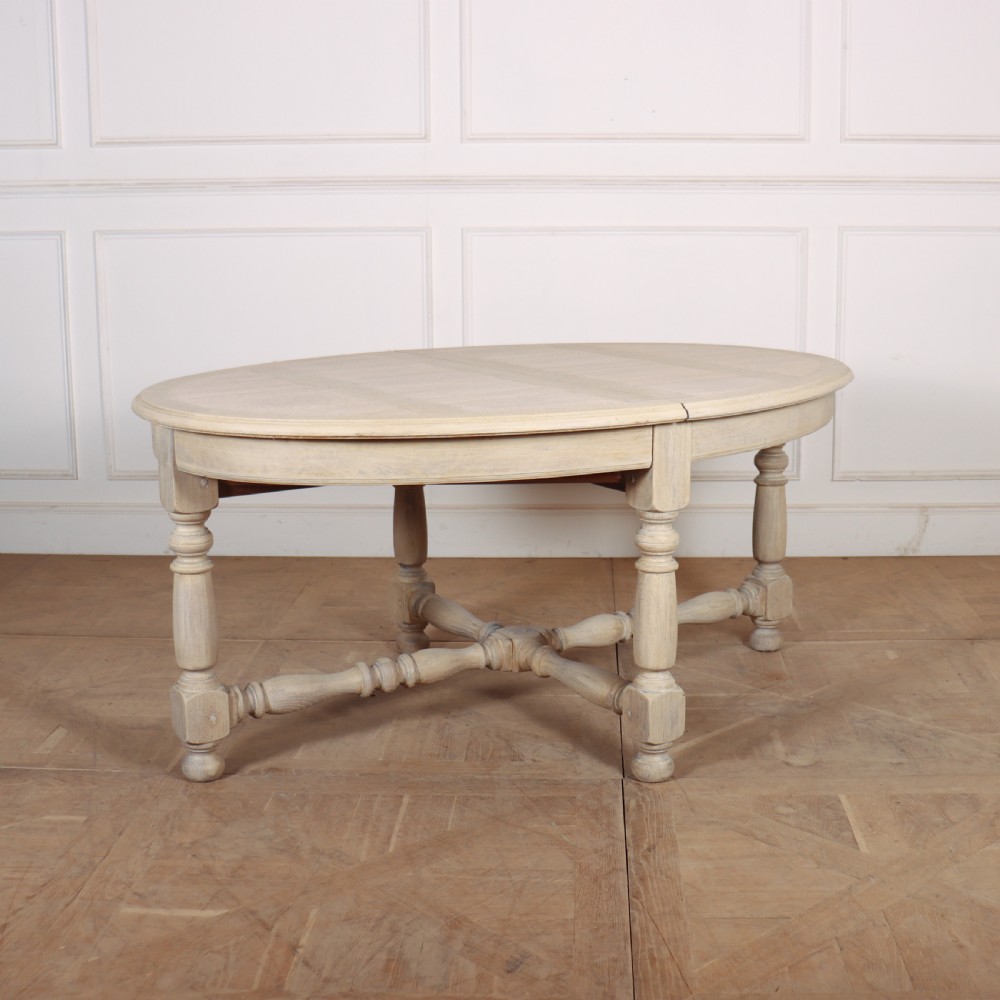 An oval bleached oak dining table with turned legs and an X-shaped lower stretcher. View II