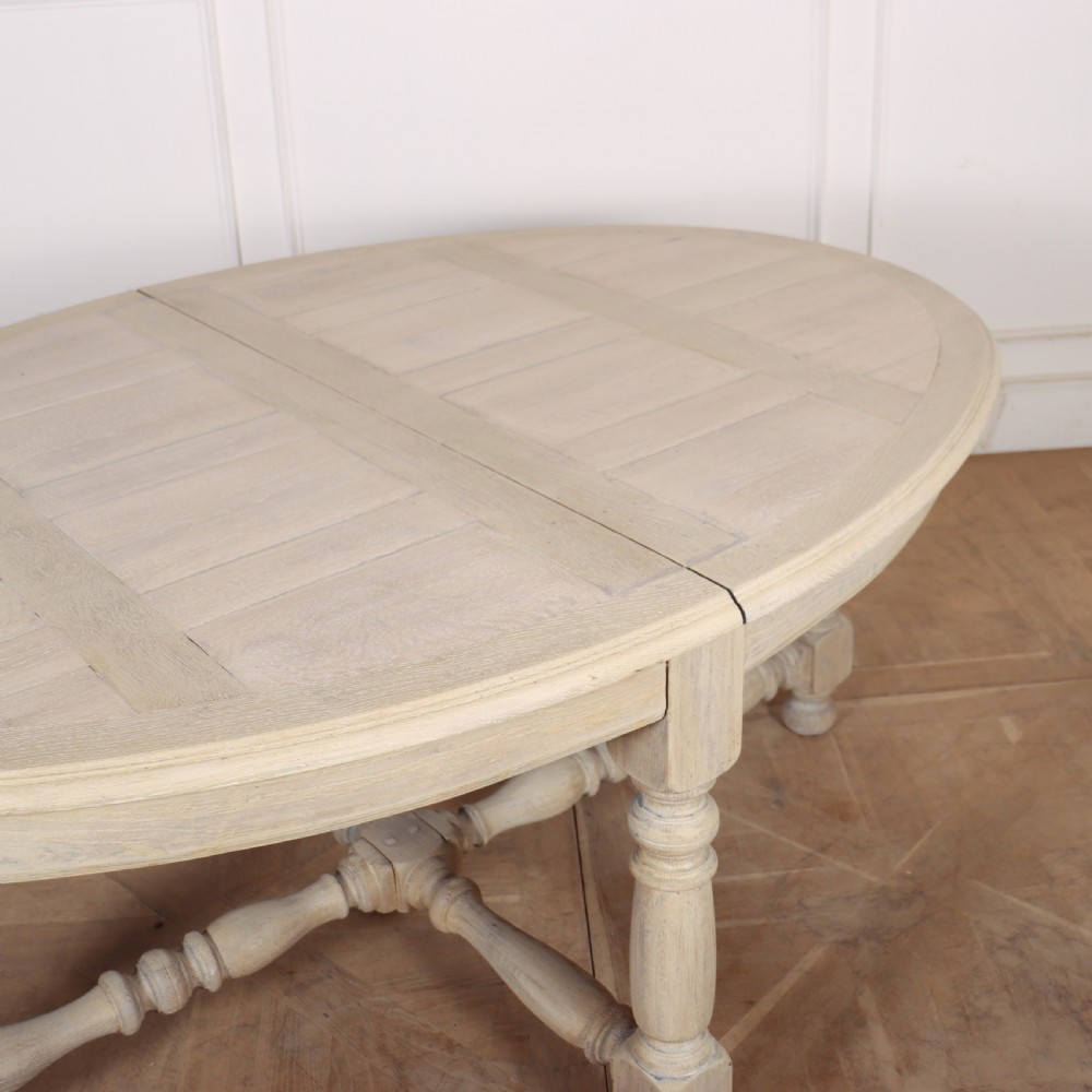 An oval bleached oak dining table with turned legs and an X-shaped lower stretcher. View III