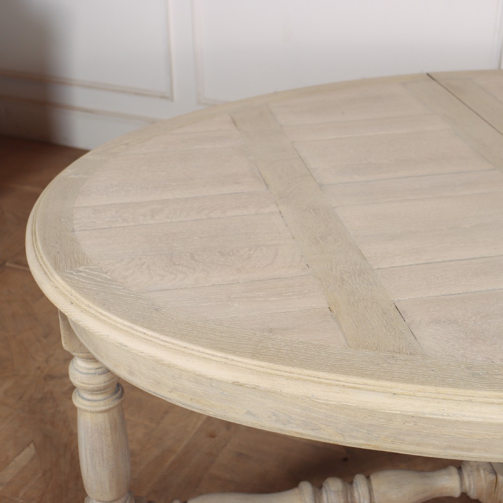 An oval bleached oak dining table with turned legs and an X-shaped lower stretcher. View IV