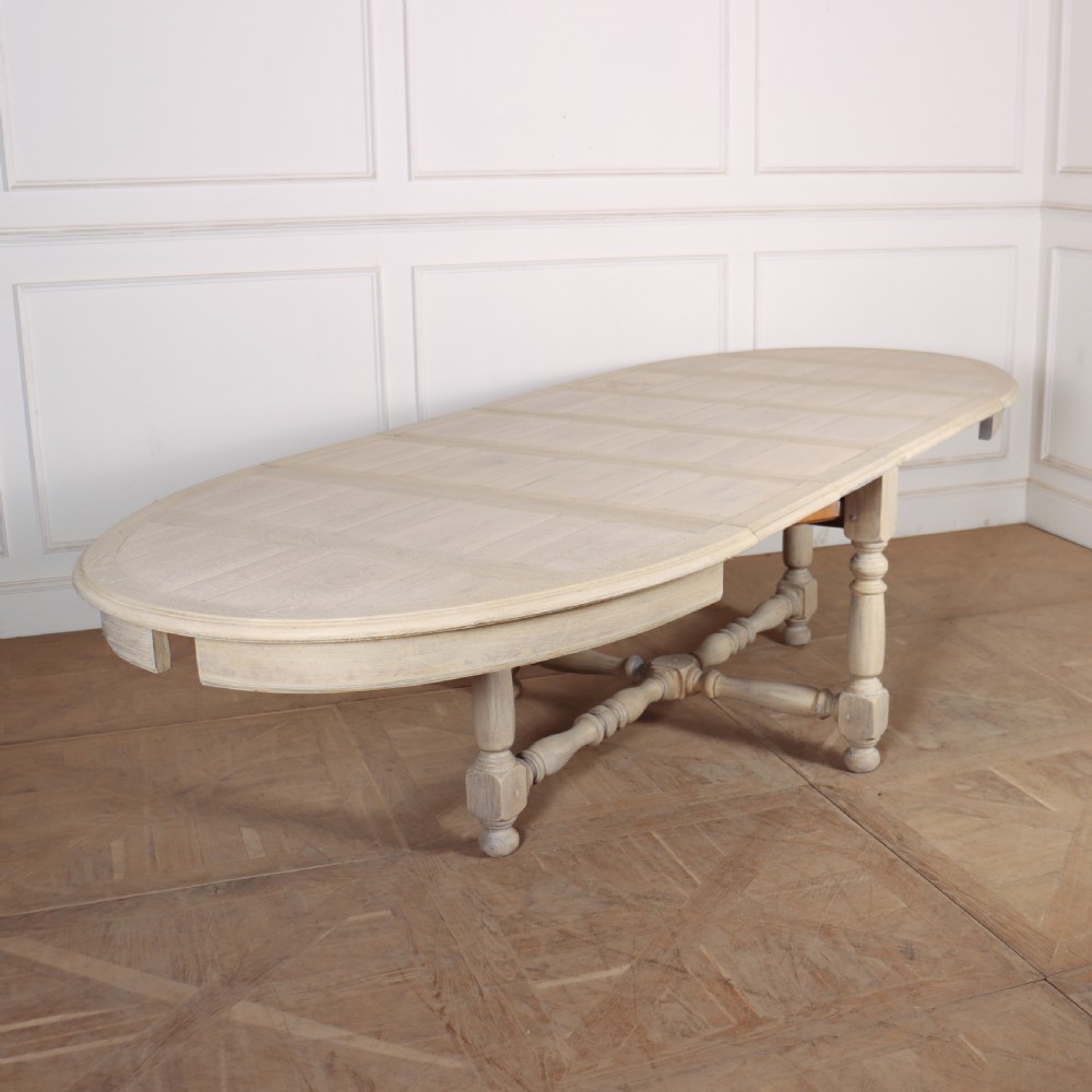 An oval bleached oak dining table with turned legs and an X-shaped lower stretcher. View V