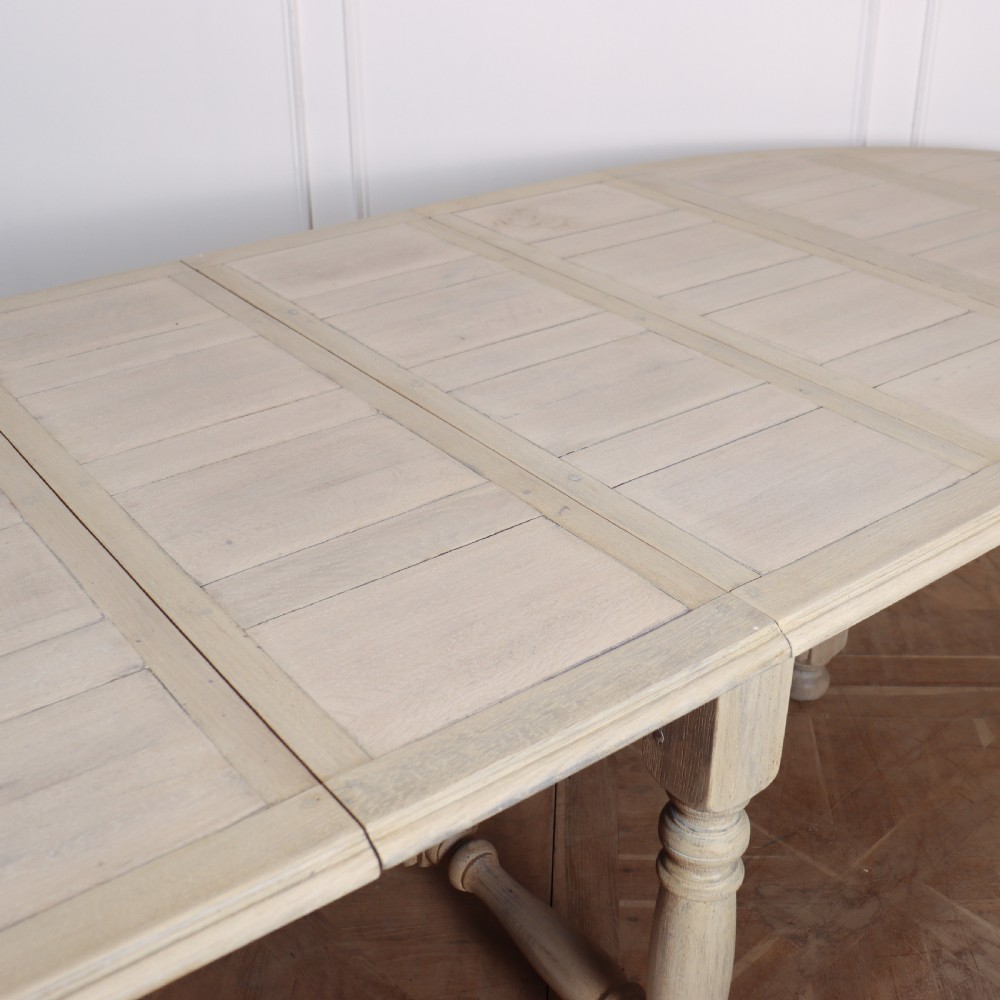 An oval bleached oak dining table with turned legs and an X-shaped lower stretcher. View VI