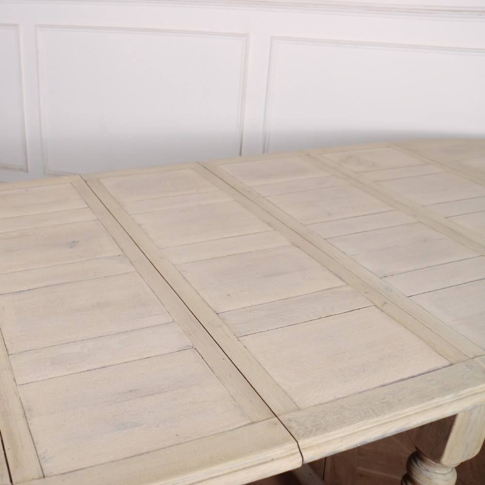An oval bleached oak dining table with turned legs and an X-shaped lower stretcher. View VII