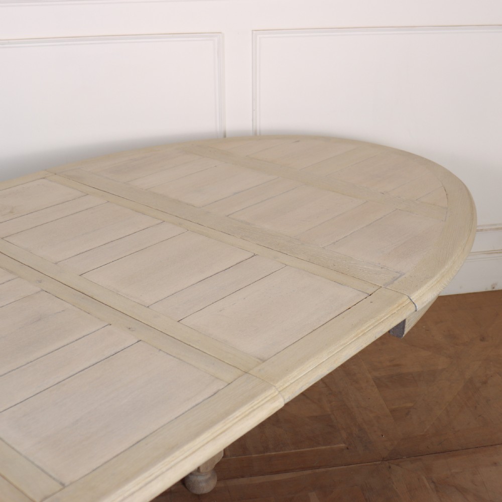 An oval bleached oak dining table with turned legs and an X-shaped lower stretcher. View VIII