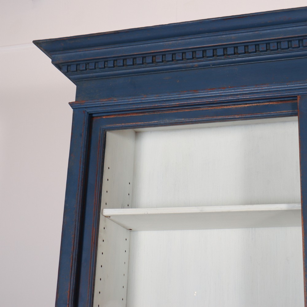 A large two-tier blue painted display cabinet featuring sliding glass doors and a white painted interior fitted with shelves. View II