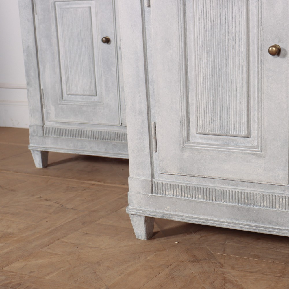 A pair of Swedish enfilades featuring a distressed pale grey painted finish, panelled cupboard doors, small round brass knobs, and short tapered legs. View VII