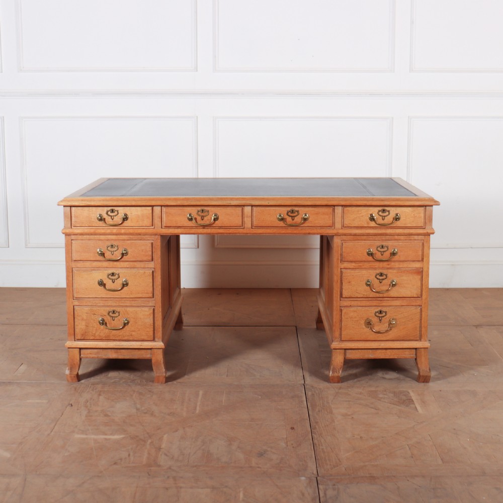 An antique pale oak pedestal desk featuring ten drawers with brass drop handles and a dark leather inset writing surface.