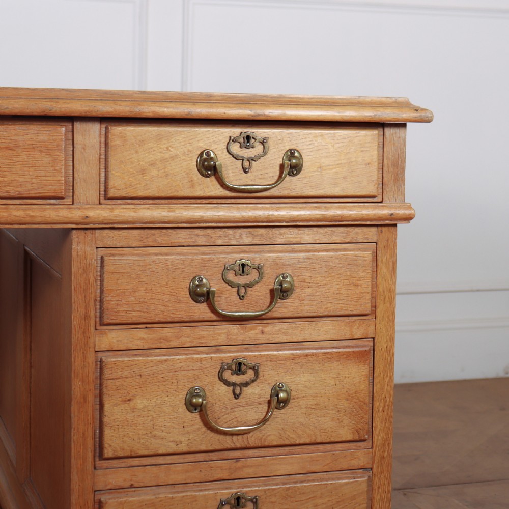 An antique pale oak pedestal desk featuring ten drawers with brass drop handles and a dark leather inset writing surface. View II